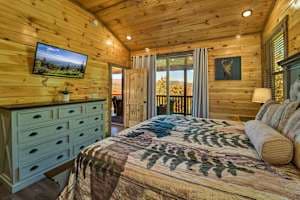 Escape to this cozy bedroom with a king-size bed, private bathroom, closet, dresser, and TV. Step onto the deck to enjoy stunning views and fresh mountain air. Designed for comfort and relaxation, this serene retreat is perfect after a long day.