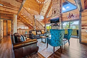 Relax in the stunning cabin-style living room featuring vaulted ceilings, a stone fireplace, and large windows with scenic views. Plush leather seating and rustic decor create a cozy yet elegant retreat—perfect for gathering with family and friends!