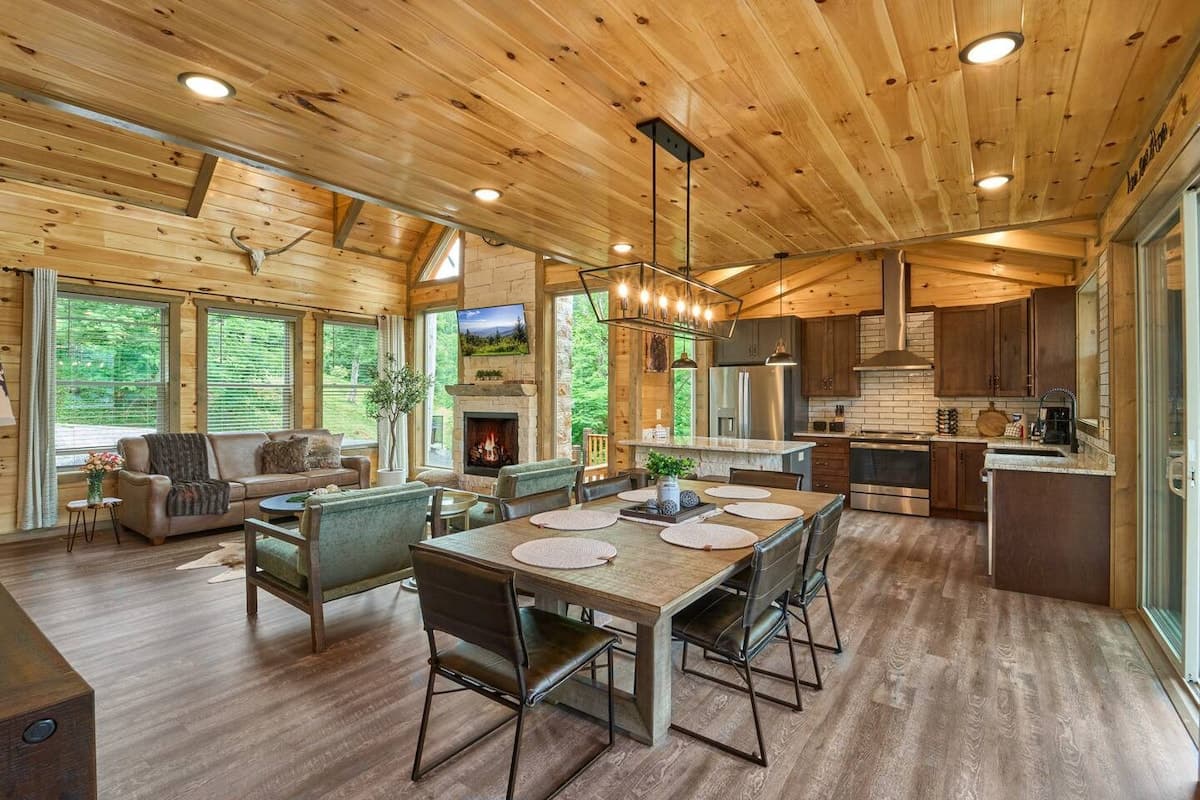 Spacious open-concept living with a dining table for six plus three additional seats at the kitchen island. Enjoy a cozy fireplace, modern kitchen, and large windows with serene views. Perfect for family gatherings and relaxing mountain getaways!