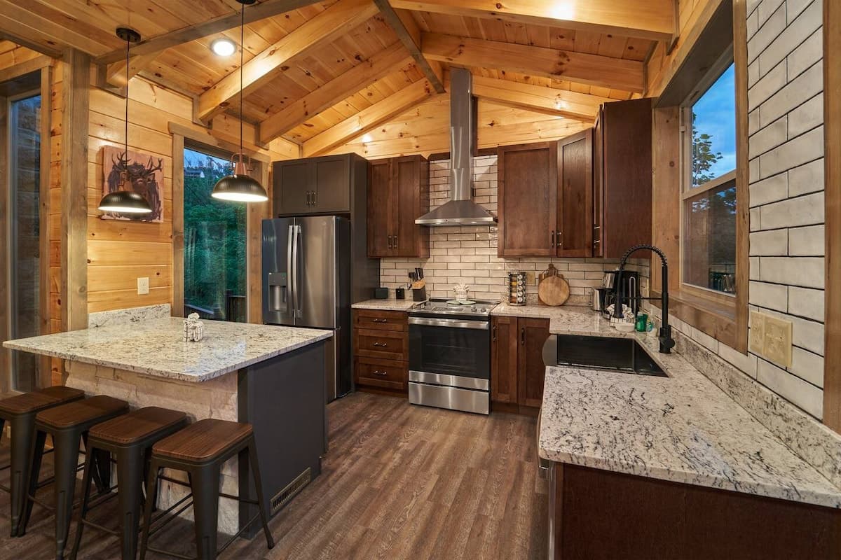 Modern rustic kitchen with granite countertops, stainless steel appliances, and a spacious island with seating for four. Fully equipped for home-cooked meals and family gatherings in a cozy cabin setting. A perfect blend of style and convenience!