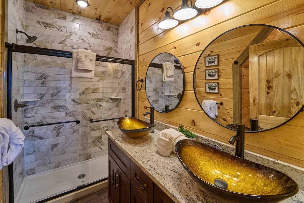 This full bathroom offers modern comfort with fresh towels, toilet paper, hand soap, body soap, and a hair dryer. Featuring a walk-in shower, granite vanity, and cozy cabin charm, it's stocked with essentials to ensure a refreshing & hassle-free stay