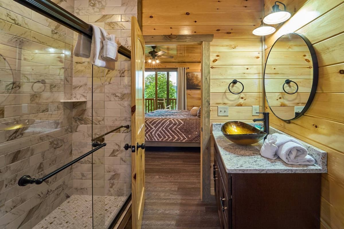 This full bathroom offers modern comfort with fresh towels, toilet paper, hand soap, body soap, and a hair dryer. Featuring a walk-in shower, granite vanity, and cozy cabin charm, it's stocked with essentials to ensure a refreshing & hassle-free stay