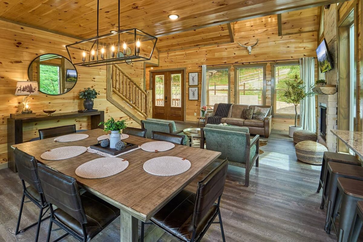Spacious open-concept living with a dining table for six plus three additional seats at the kitchen island. Enjoy a cozy fireplace, modern kitchen, and large windows with serene views. Perfect for family gatherings and relaxing mountain getaways!