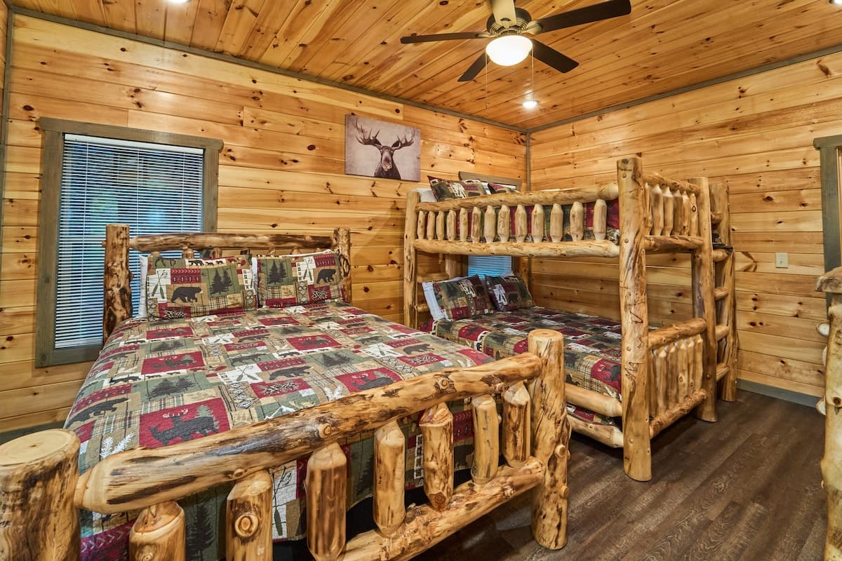 This rustic bedroom features a queen bed and a log-style bunk bed, perfect for families or groups. Enjoy a private full bathroom, dresser, and direct deck access. Cozy cabin décor and modern comforts make it a relaxing retreat after a fun-filled day!