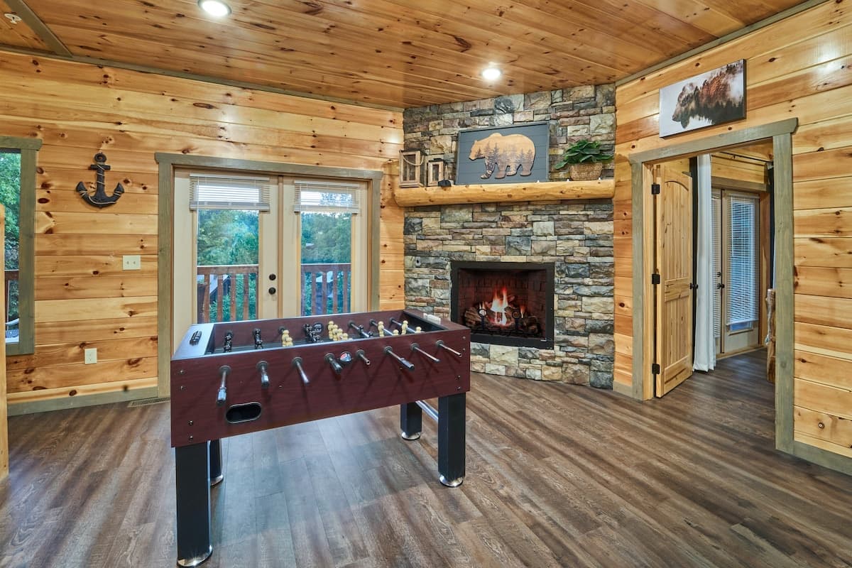 Enjoy a game of foosball in this cozy cabin space featuring two fireplaces for the perfect mix of fun and relaxation. With rustic charm and warm ambiance, this inviting area is great for friendly competition or unwinding by the fire after a long day!