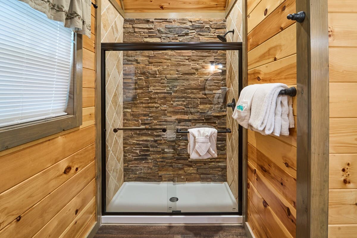 This full bathroom offers modern comfort with fresh towels, toilet paper, hand soap, body soap, and a hair dryer. Featuring a walk-in shower, granite vanity, and cozy cabin charm, it's stocked with essentials to ensure a refreshing & hassle-free stay