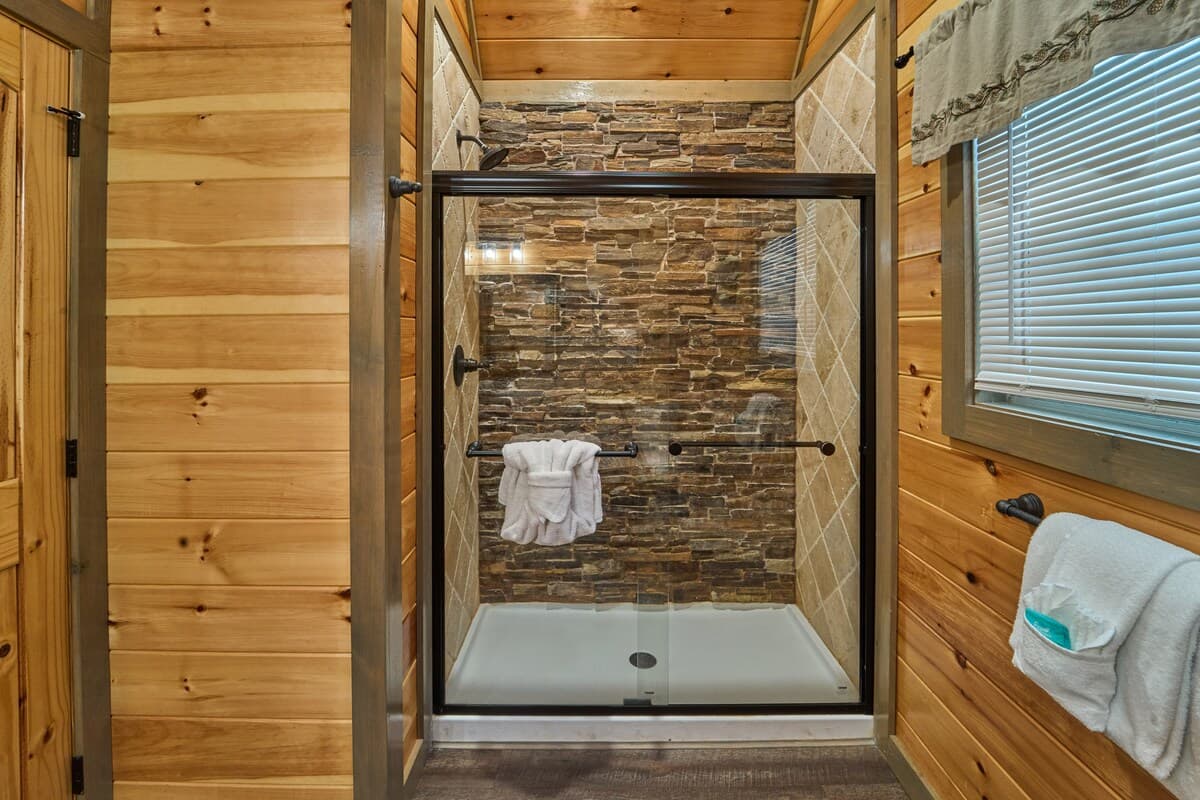 This full bathroom offers modern comfort with fresh towels, toilet paper, hand soap, body soap, and a hair dryer. Featuring a walk-in shower, granite vanity, and cozy cabin charm, it's stocked with essentials to ensure a refreshing & hassle-free stay