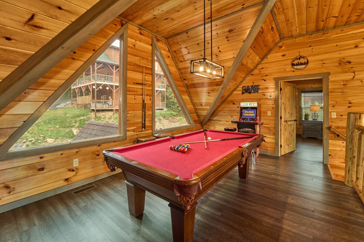 Challenge friends to a game of pool in this stylish loft game area with vaulted ceilings and scenic views. Featuring a cozy cabin atmosphere and classic arcade décor, it's the perfect space to relax, have fun, and enjoy friendly competition!
