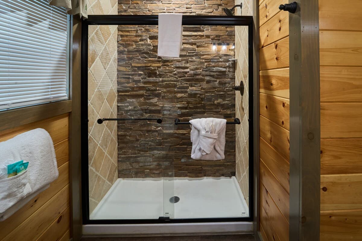 This full bathroom offers modern comfort with fresh towels, toilet paper, hand soap, body soap, and a hair dryer. Featuring a walk-in shower, granite vanity, and cozy cabin charm, it's stocked with essentials to ensure a refreshing & hassle-free stay