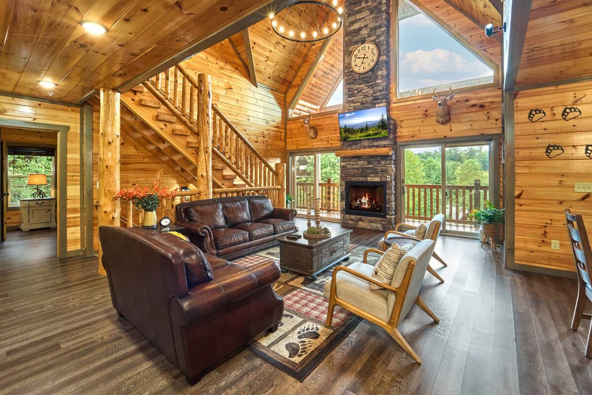 Relax in the stunning cabin-style living room featuring vaulted ceilings, a stone fireplace, and large windows with scenic views. Plush leather seating and rustic decor create a cozy yet elegant retreat—perfect for gathering with family and friends!