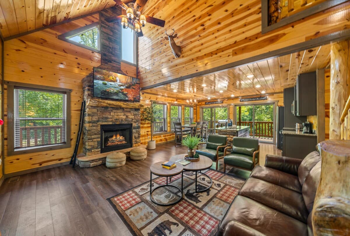 Unwind in this cozy cabin-style living room with vaulted wood ceilings, a stone gas fireplace, and scenic forest views! Enjoy plush seating and an open layout, perfect for families / groups. This rustic yet modern retreat offers warmth and comfort.