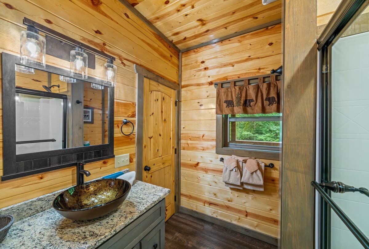 This full bathroom offers modern comfort with fresh towels, toilet paper, hand soap, body soap, and a hair dryer. Featuring a walk-in shower, granite vanity, and cozy cabin charm, it's stocked with essentials to ensure a refreshing & hassle-free stay