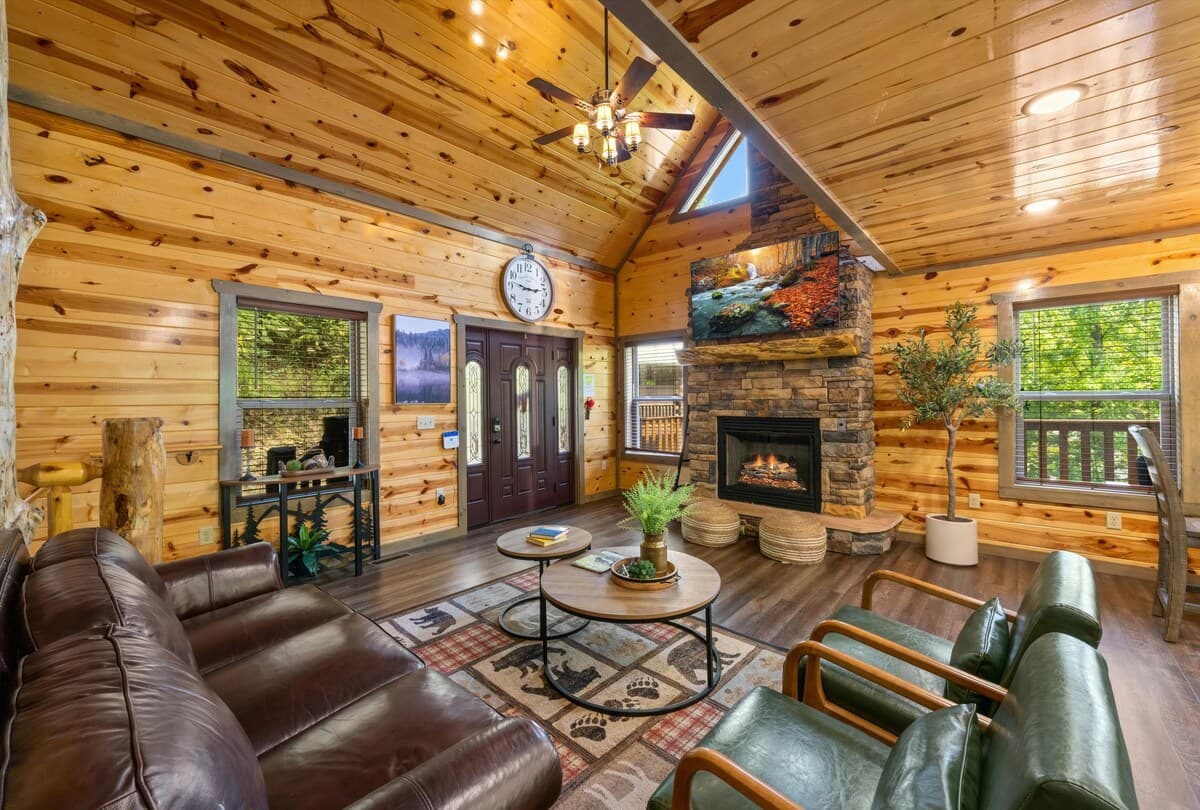 Unwind in this cozy cabin-style living room with vaulted wood ceilings, a stone gas fireplace, and scenic forest views! Enjoy plush seating and an open layout, perfect for families / groups. This rustic yet modern retreat offers warmth and comfort.