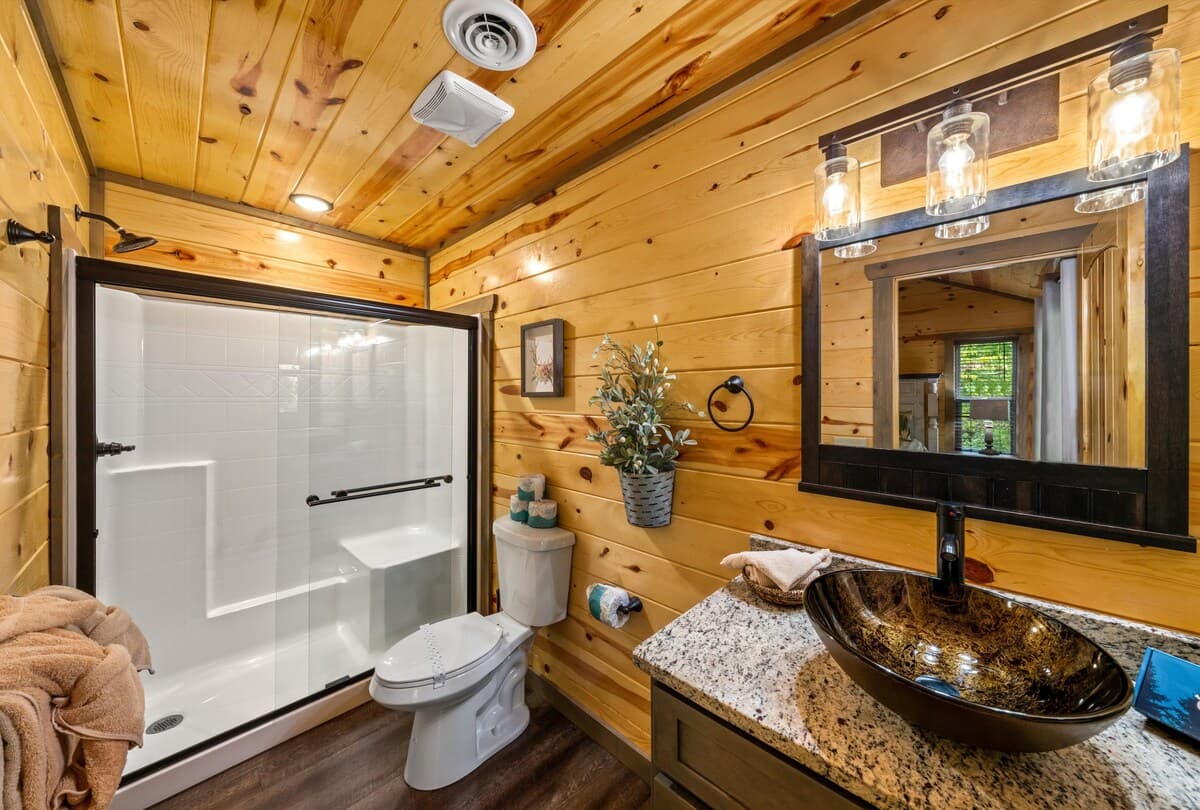 This full bathroom offers modern comfort with fresh towels, toilet paper, hand soap, body soap, and a hair dryer. Featuring a walk-in shower, granite vanity, and cozy cabin charm, it's stocked with essentials to ensure a refreshing & hassle-free stay