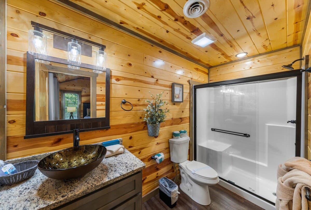 This full bathroom offers modern comfort with fresh towels, toilet paper, hand soap, body soap, and a hair dryer. Featuring a walk-in shower, granite vanity, and cozy cabin charm, it's stocked with essentials to ensure a refreshing & hassle-free stay